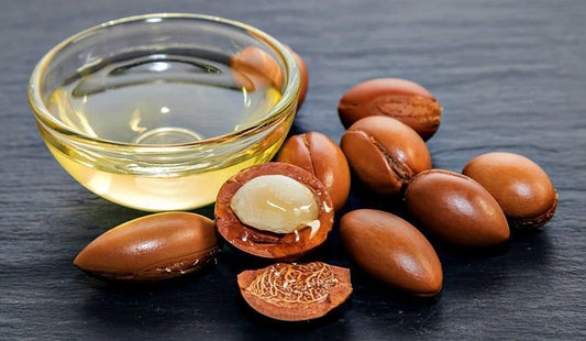 Argan oil in a transparent glass bowl with cracked open argan seed next to the oil on a black surface