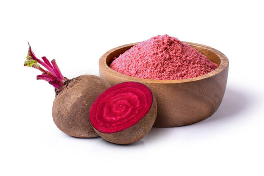Beetroot powder in a brown wooden bowl with a half cut beetroot plant next to it on a white surface