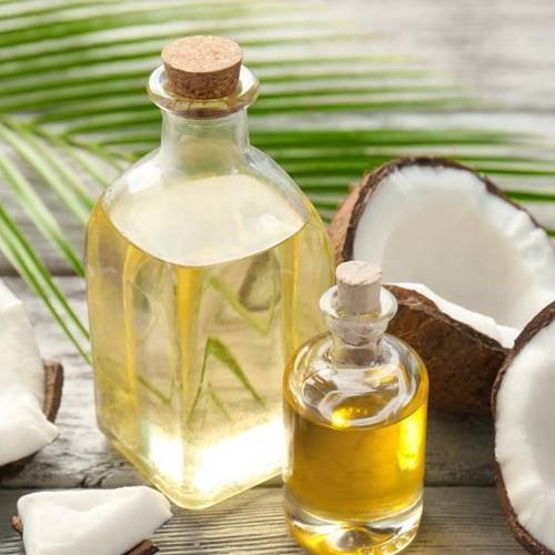 Coconut oil in two transparent glass bottles with coconuts on a table 