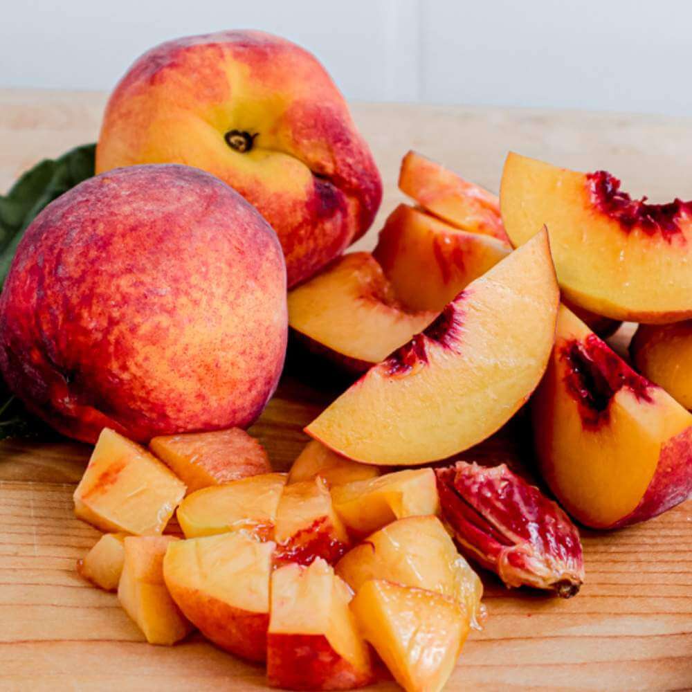 2 peach fruits and diced peaches on a wooden surface