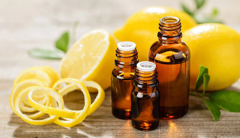 lemon essential oil in 3 amber bottle. Two small bottles with euro dropper caps and one with with half cut lemon on a wooden table