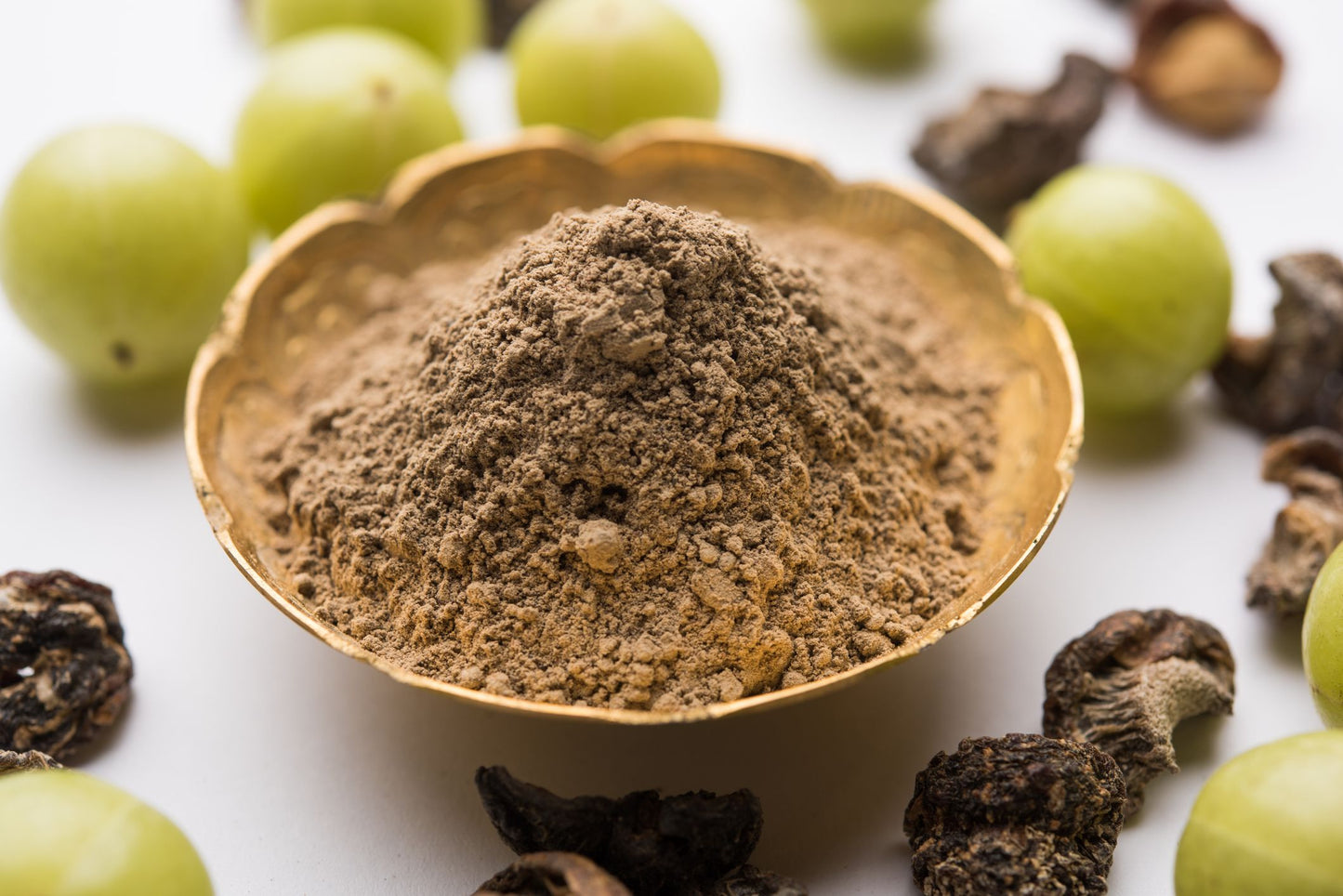 Amla powder in a brown clay bow surrounded by green fresh amla fruits and dried brown amla seeds