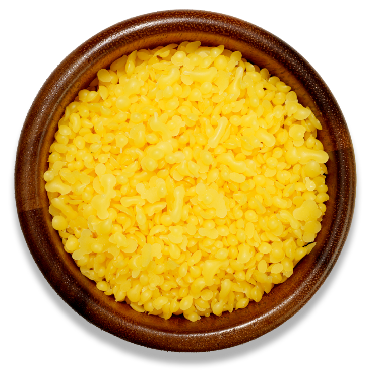 Yellow beeswax pellets in a brown wooden bowl on a transparent surface 