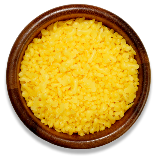 Yellow beeswax pellets in a brown wooden bowl on a transparent surface 