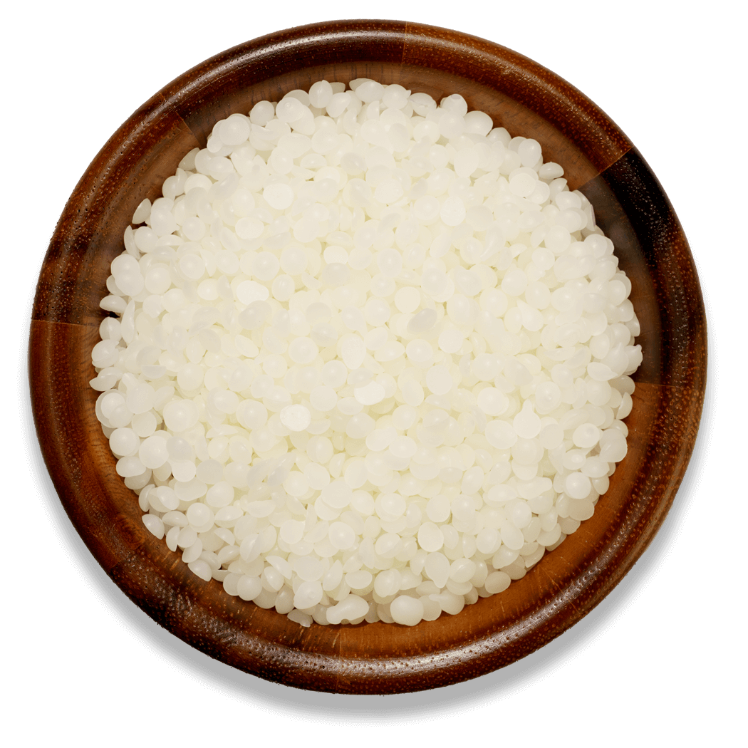White beeswax pellets in a wooden bowl on a white surface