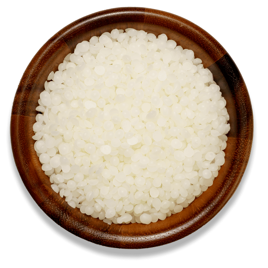 White beeswax pellets in a wooden bowl on a white surface 