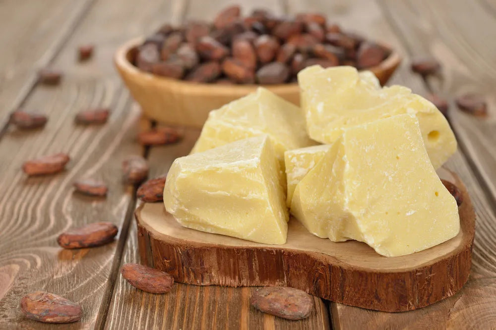 Raw Cocoa Butter chunks on a wooden base with cocoa pods in a wooded plate 