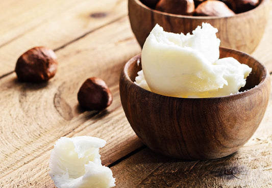 Raw shea butter in a wooden bowl and shea nuts in another wooden bowl on a wooden surface