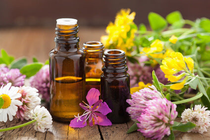 3 amber bottles, one half full of oil surrounded by flowers on a wooden surface 