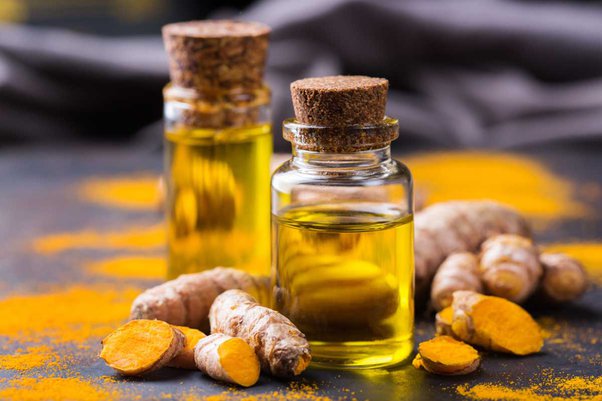 Turmeric oil in a two transparent glass bottles with cork lid on a dark surface with turmeric root and turmeric powder 